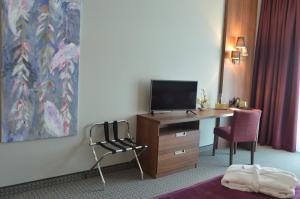 Habitación de hotel con escritorio, TV y silla. en Sante Royale Hotel- & Gesundheitsresort Bad Langensalza en Bad Langensalza