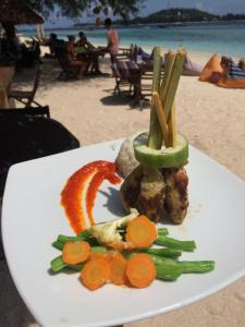a plate of food with meat and vegetables on the beach at Gili Beach in Gili Meno