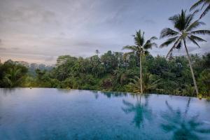 a swimming pool in front of a forest with palm trees at Natya Resort Ubud in Ubud