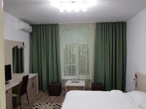 1 dormitorio con cortinas verdes, 1 cama y escritorio en Lorena Apart Old Town, en Bucarest