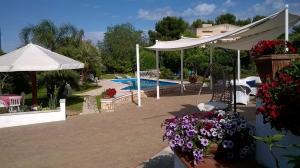 eine Terrasse mit einem Pool, einem weißen Sonnenschirm und Blumen in der Unterkunft B&B Le Vele in Maruggio