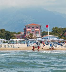 a beach with chairs and umbrellas and a pink building at Hotel Happy in Marina di Pietrasanta