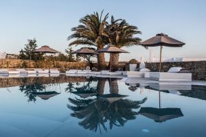 a beach with a pool, chairs, and tables at Ostraco Suites in Mikonos