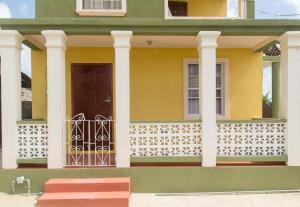 a yellow house with a door and a fence at Believe Caribbean Apartment in Bridgetown