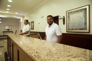 two men standing behind a counter in a waiting room at Real Palace Hotel in Santa Rita do Sapucaí