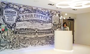 a woman standing behind a podium in front of a wall covered in posters at Point A Hotel London Shoreditch in London