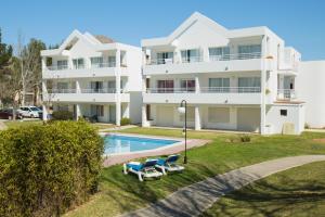 a large white house with a swimming pool and two lawn chairs at Apartamentos Habitat in Port de Pollensa