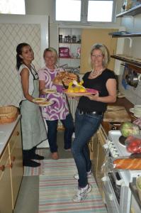 three women standing in a kitchen holding a plate of food at Tivedens Hostel-Vandrarhem in Karlsborg