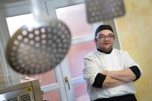 un chef debout dans une cuisine avec les bras croisés dans l'établissement Hotel Palazzo Di Mezzo, à Carrù