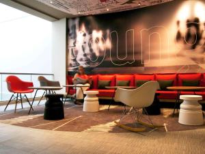 a man sitting on a red couch in a room with tables and chairs at Hotel ibis Lisboa Saldanha in Lisbon