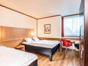 um quarto de hotel com duas camas e uma cadeira vermelha em ibis Hotel Eisenach em Eisenach