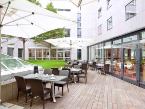 eine Außenterrasse mit Tischen, Stühlen und Sonnenschirmen in der Unterkunft voco Dusseldorf Seestern, an IHG Hotel in Düsseldorf
