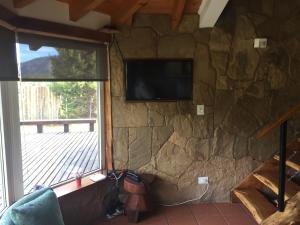 a room with a stone wall with a television and a window at Inpeuma meliquina in Villa Meliquina