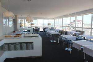 a restaurant with white tables and chairs and windows at Costa de Prata Hotel in Figueira da Foz