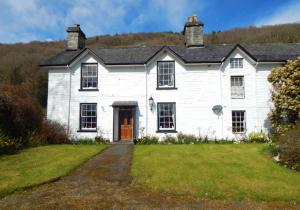 a white house with a door and a grass yard at Gogarth hall Farm holidays in Pennal