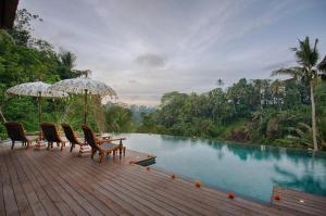 a wooden deck with chairs and a swimming pool at Natya Resort Ubud in Ubud