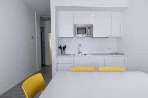 una cocina blanca con 2 sillas amarillas y lavamanos en Bertamini Apartments, en Nago-Torbole