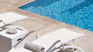 two white chairs next to a swimming pool at Mykonos Panormos Villas in Mykonos
