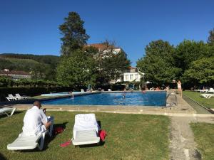a man sitting in lawn chairs in front of a swimming pool at Balneario Acuña in Caldas de Reis