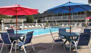 two tables and chairs with umbrellas in front of a pool at Cape Harbor Motor Inn in Cape May