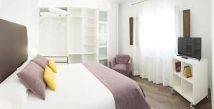 1 dormitorio con 1 cama blanca y TV en AiA EXCLUSIVE APARTMENTS, en Granada