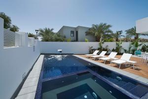 a swimming pool with white chairs and a house at Villa Gardenya in Eilat