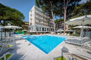 a pool with chairs and umbrellas in front of a building at Hotel San Marco in Milano Marittima