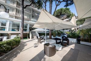 eine Terrasse mit Tischen, Stühlen und einem Sonnenschirm in der Unterkunft Hotel San Marco in Milano Marittima