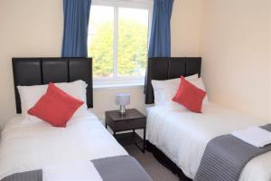 a bedroom with two beds with red pillows and a window at Kelpies Serviced Apartments Alexander- 2 Bedrooms in Falkirk