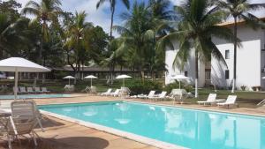 a pool with chairs and umbrellas and palm trees at Flat Ilhéus - Jubiabá Olivença in Ilhéus