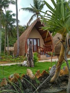 a small house with a thatched roof and palm trees at Karimun Lumbung in Karimunjawa