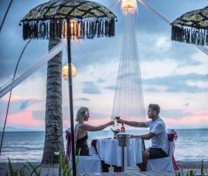 a man and a woman sitting at a table on the beach at The Chandi Boutique Resort & Spa in Senggigi