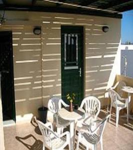 un patio con sillas blancas, una mesa y una puerta verde en Pension Stella, en Naxos Chora