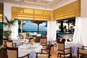 un restaurante con mesas y sillas blancas y vistas al océano en Constantinou Bros Athena Beach Hotel en Pafos