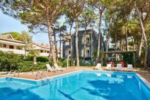 a swimming pool with chairs and a house in the background at G/Hotel Lignano in Lignano Sabbiadoro