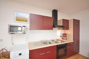 a kitchen with red cabinets and a sink and a microwave at Apartment Neuensien 11a in Seedorf