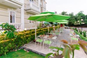 una fila de mesas y sillas con sombrillas verdes en Golden Bell Backpacker Hotel & Pool Bar, en Hoi An