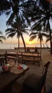 einen Sonnenuntergang am Strand mit Palmen und Tischen in der Unterkunft Tama Lodge in M'bour