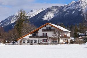 a house in the snow with mountains in the background at Ferienhotel Barmsee in Krün