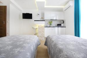 two beds in a white room with a kitchen at Apartments Madison in Zadar
