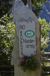 una señal en una roca con flores en ella en Ferienwohnungen Niederarnigerhof Familie Bauernfeind, en Kals am Großglockner