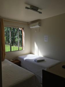 two beds in a room with a window at Hotel Texacao do Cavera in Alegrete