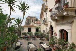 un patio con mesas, sillas y palmeras en Hotel Palazzo Krataiis, en Scilla