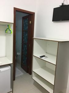 Habitación con estanterías blancas, TV y puerta en Pousada Bem Brasil, en Macaé