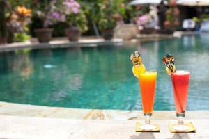two drinks sitting on a table next to a swimming pool at Tamukami Hotel in Sanur