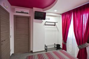シャッカにあるB&B Lido Esperando Sciaccaの赤いカーテンと壁掛けテレビ付きのベッドルーム1室