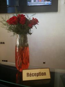 a vase with red roses on a table with a sign at Hôtel Teranga & Spa in Marrakesh