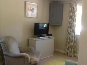 a living room with a tv and a chair at Gardeners Cottage in Crudwell