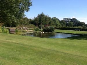 een park met een vijver en een bank in het gras bij Gardeners Cottage in Crudwell