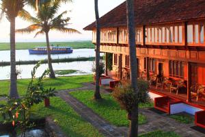 a building with a boat in the water and palm trees at Coconut Lagoon Kumarakom- a CGH Earth Experience in Kumarakom
